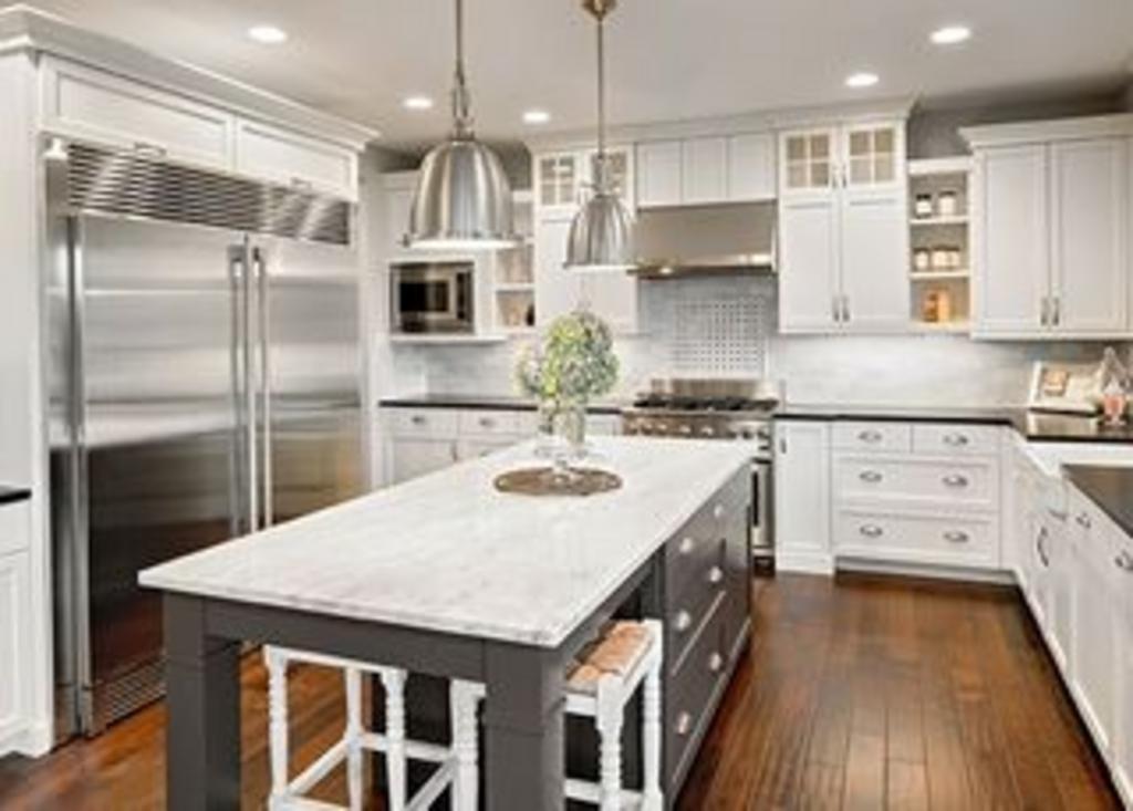 A kitchen with white cabinets and stainless steel appliances and a large island in the middle.