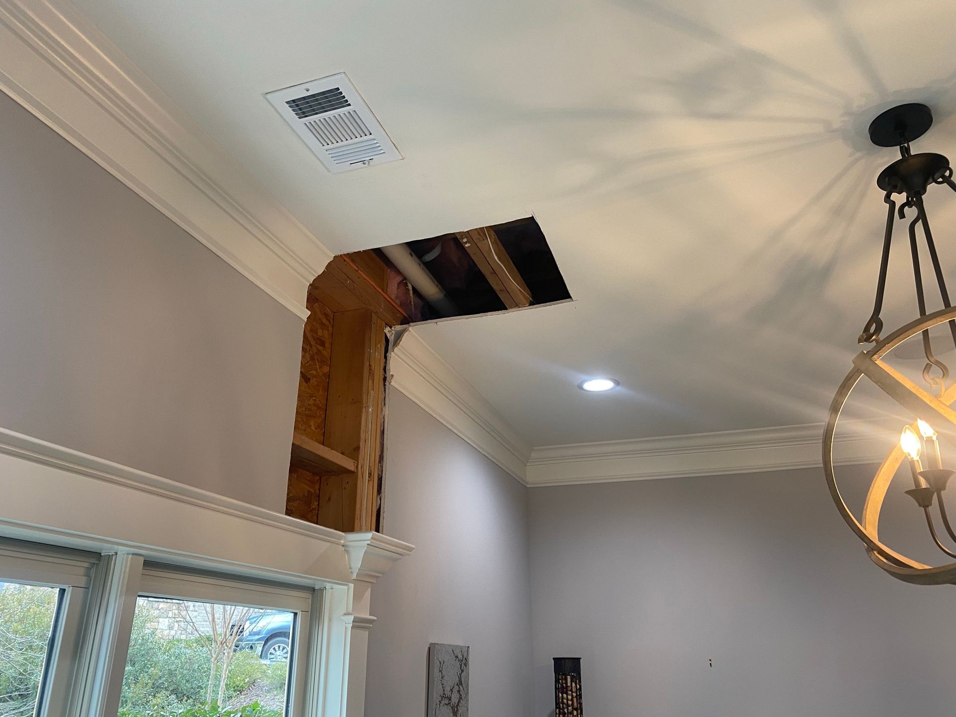 A room with a hole in the ceiling and a chandelier.