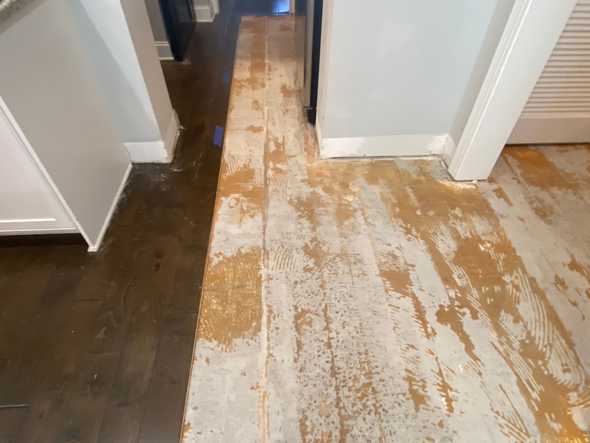 A wooden floor is being painted in a kitchen.