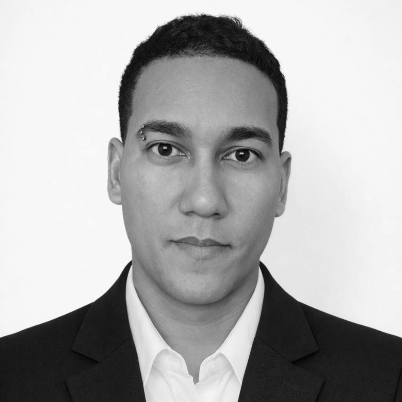 Two people smiling at the camera. Man in plaid shirt, woman in light shirt, floral backdrop.