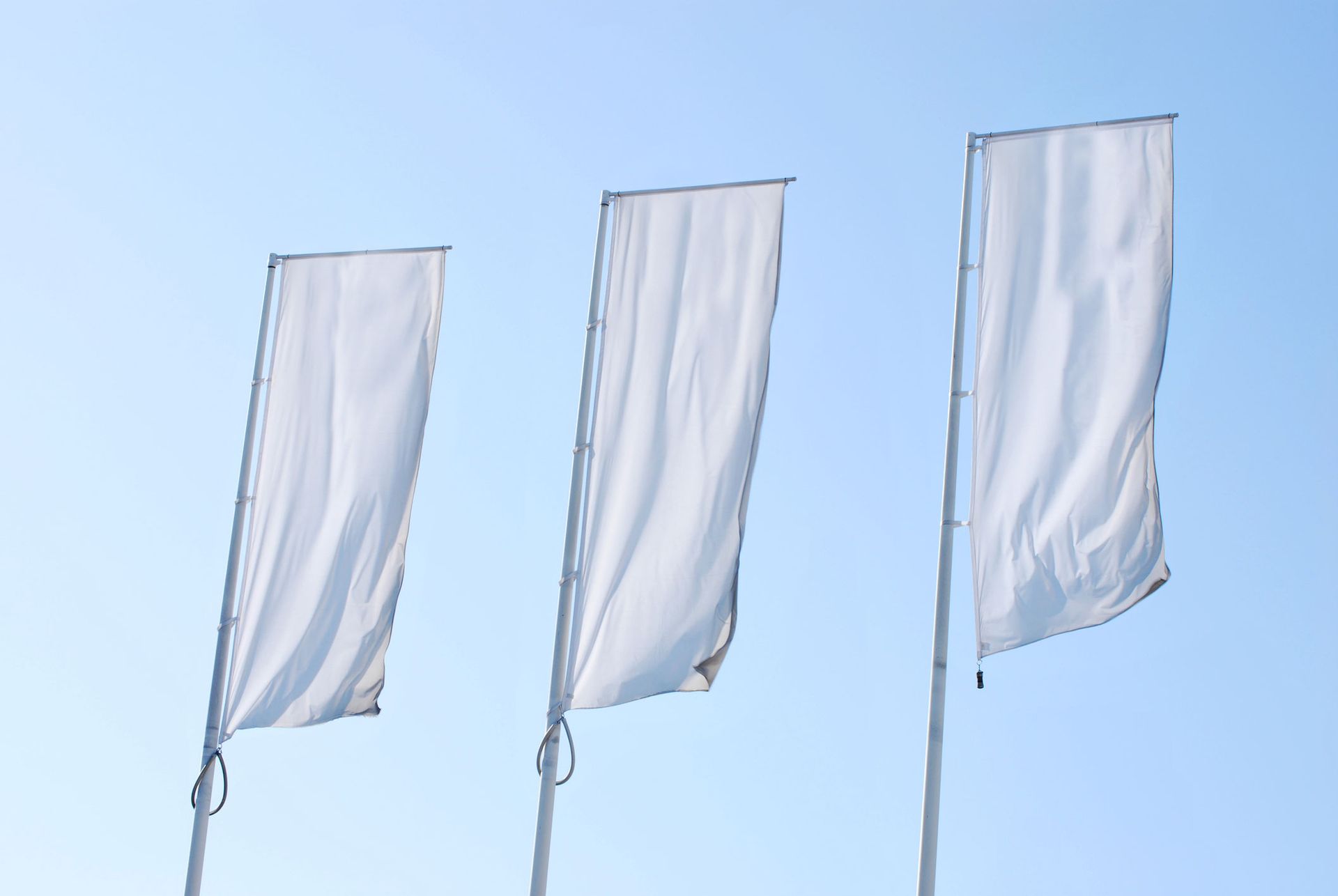 Three white flags are flying in the wind against a blue sky.