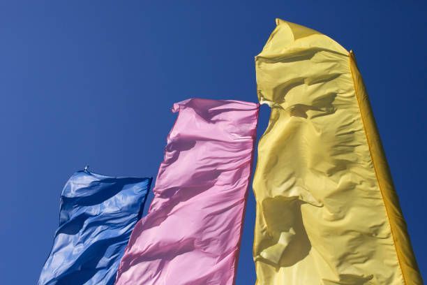 Three colorful flags are waving in the wind against a blue sky.
