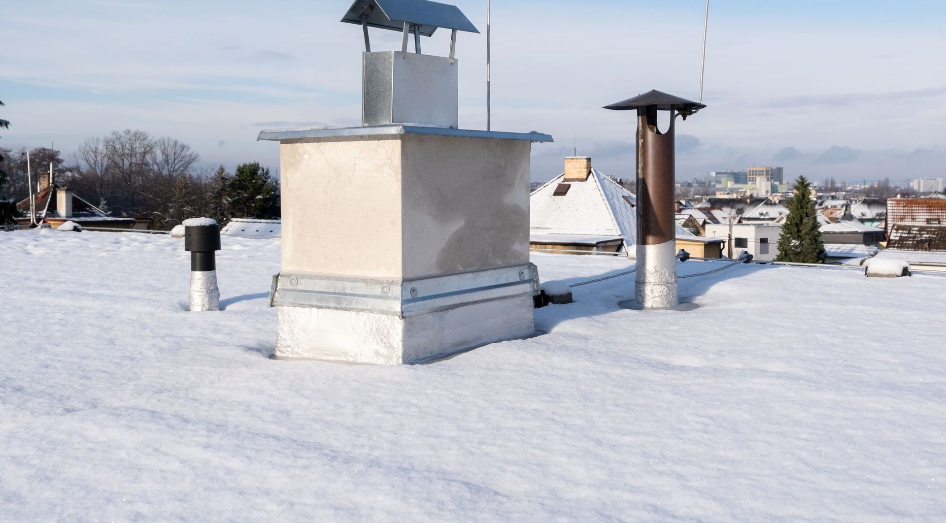 Toit recouvert de neige avec cheminées et évents contre un ciel bleu clair.