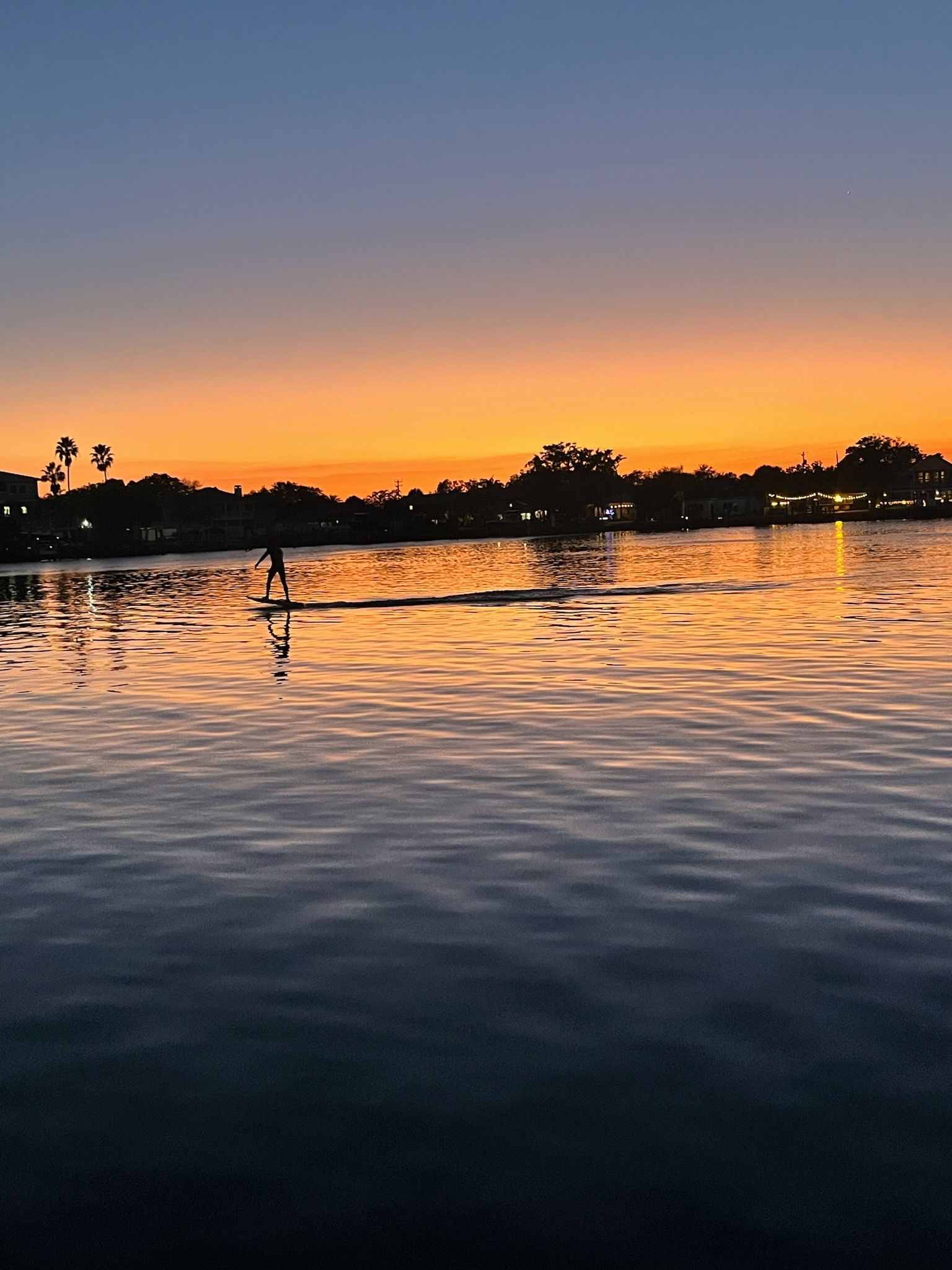 Sunset over water with person hydrofoil surfing; orange and blue sky.