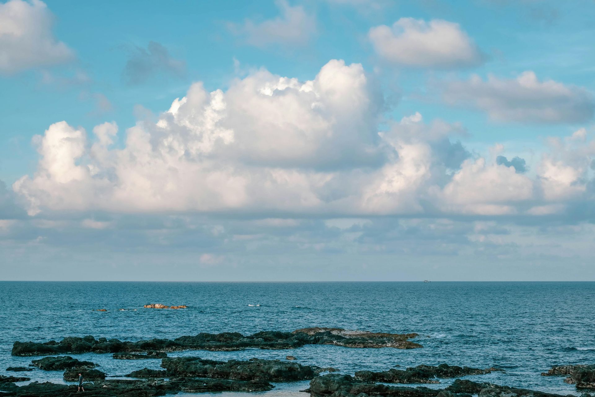 Ocean view with blue sky, white fluffy clouds, and dark rocks in the foreground. Indian shores efoil location.