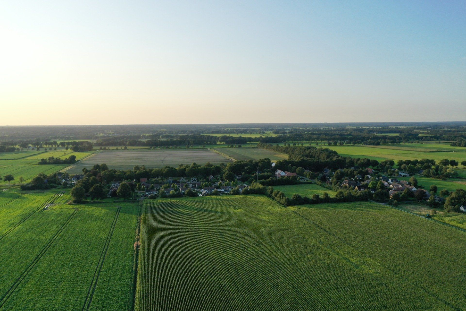 Een luchtfoto van een weelderig groen veld met in de verte een dorp.