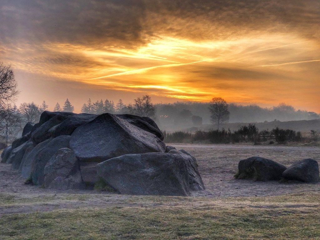 Een Drents hunebed midden in een veld met een zonsondergang op de achtergrond.