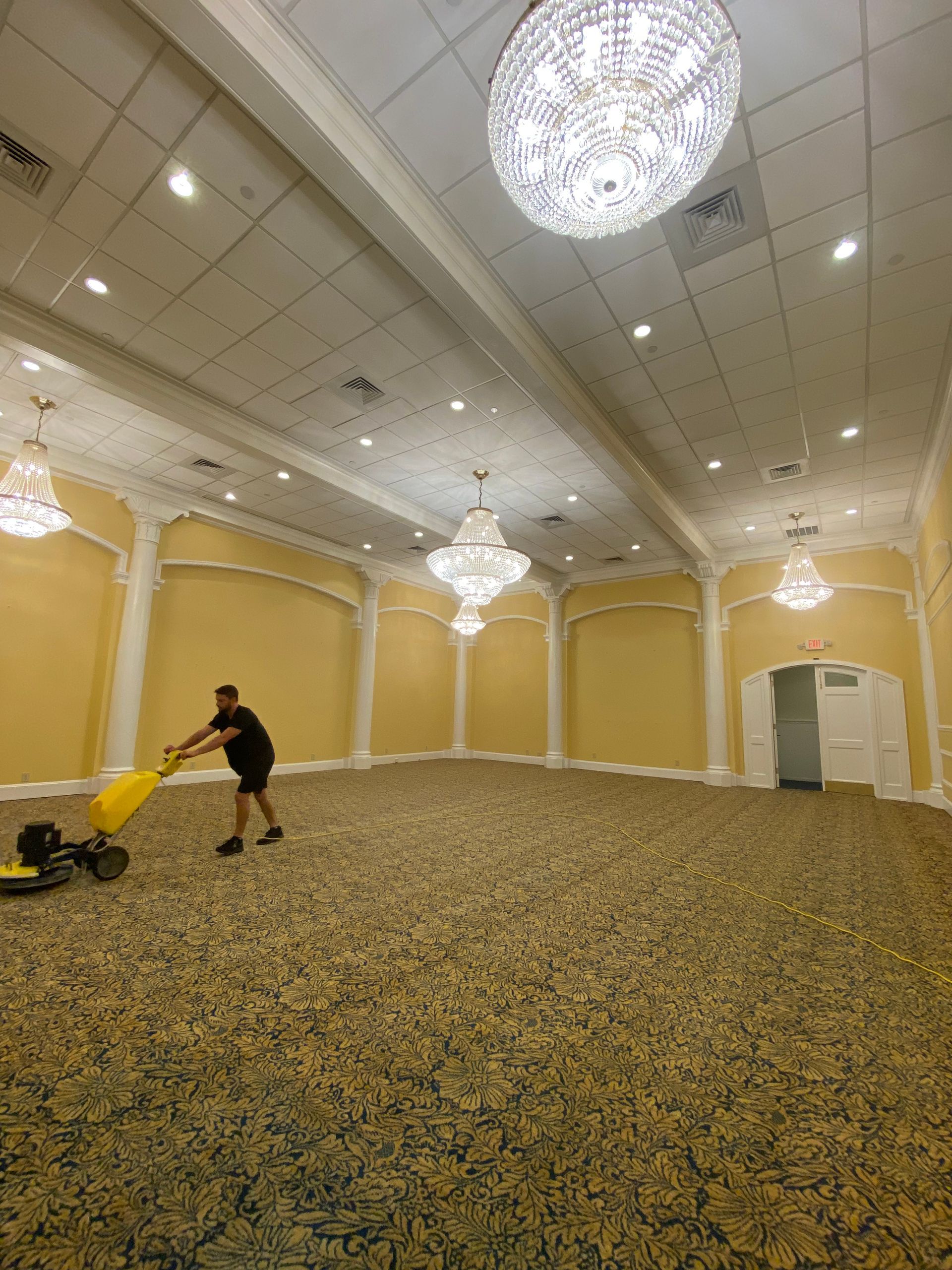 A man is cleaning a large room with a vacuum cleaner.