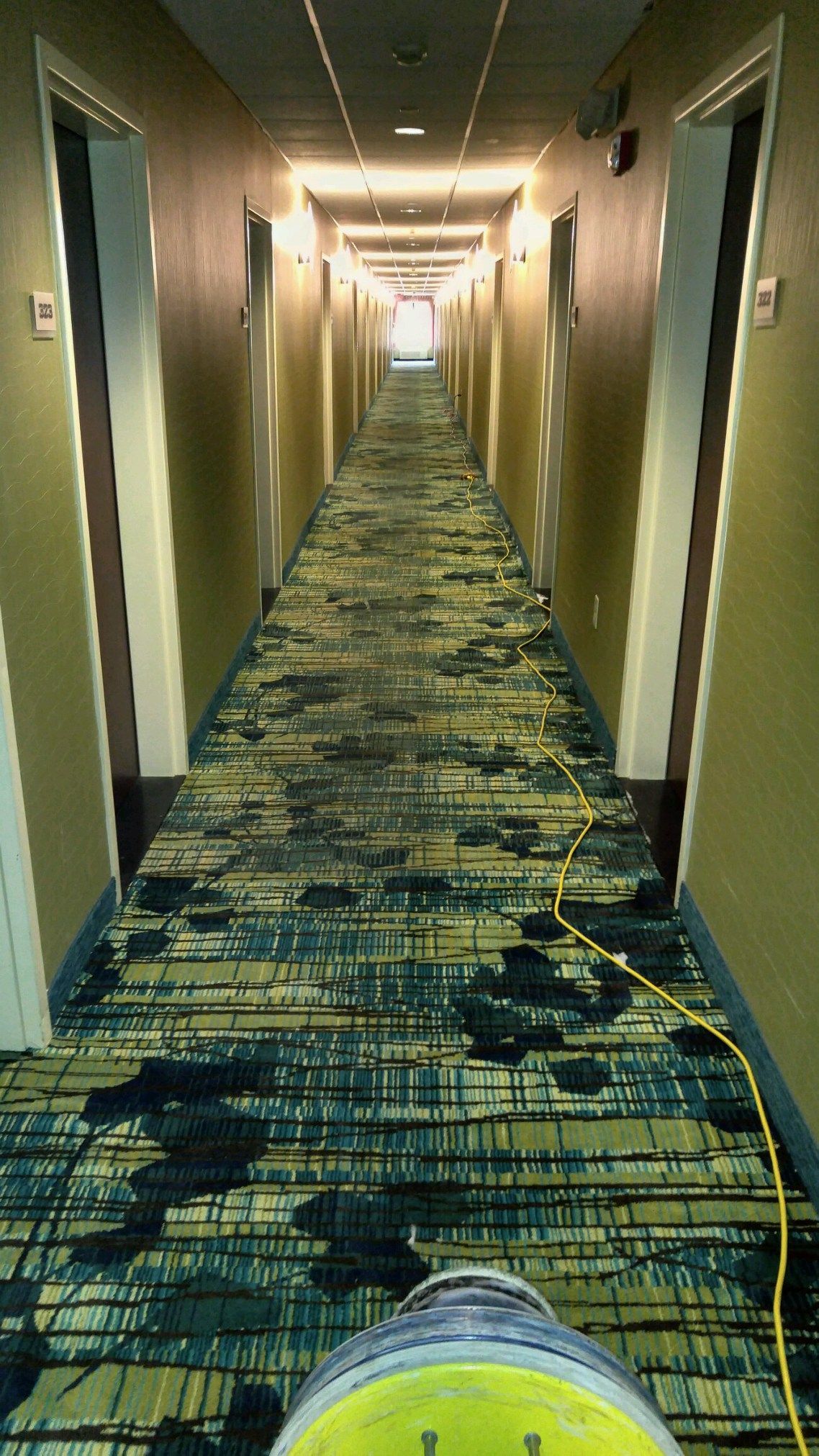 A long hallway in a hotel with a vacuum cleaner on the floor.