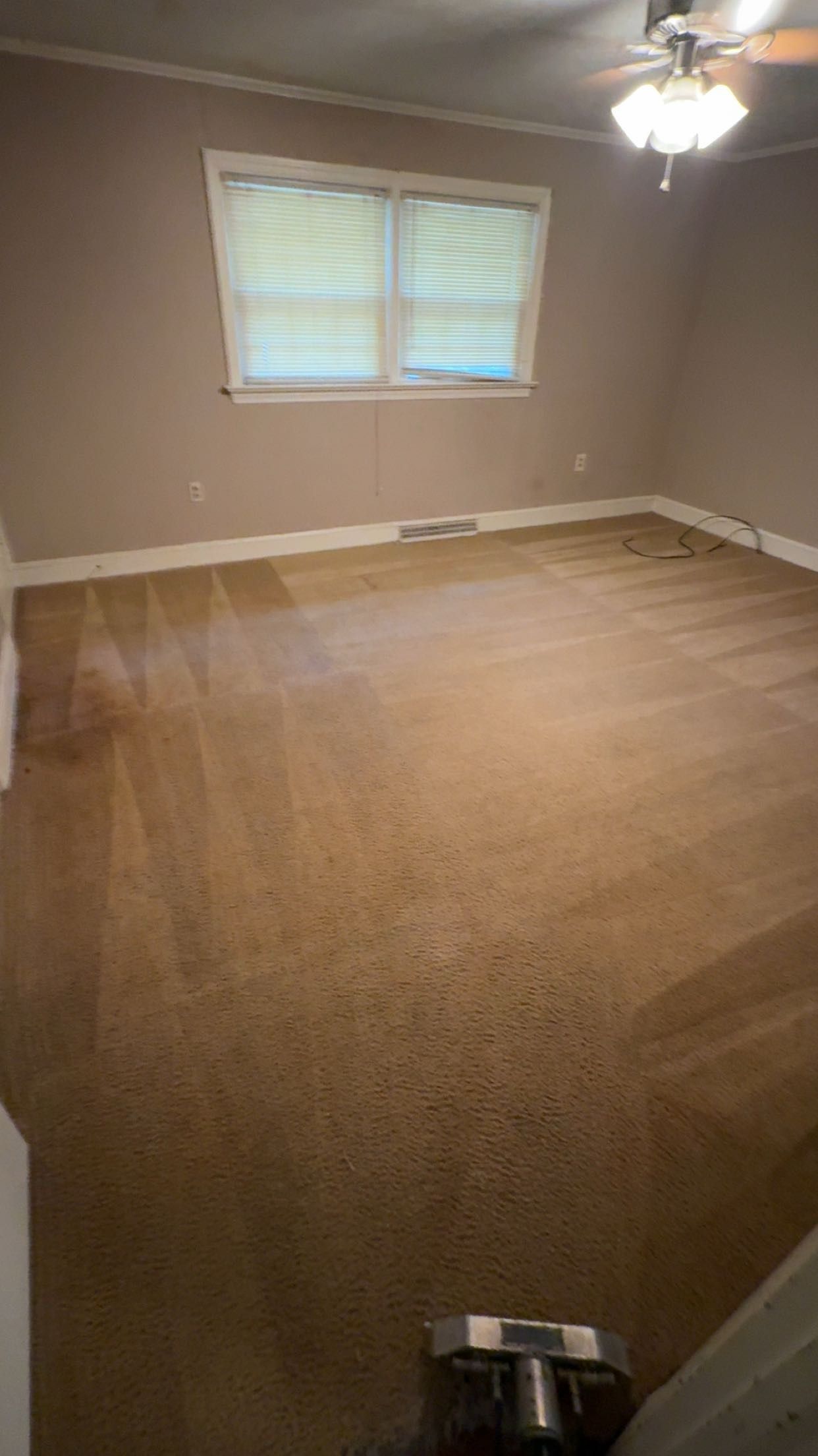 An empty living room with a ceiling fan and a window.