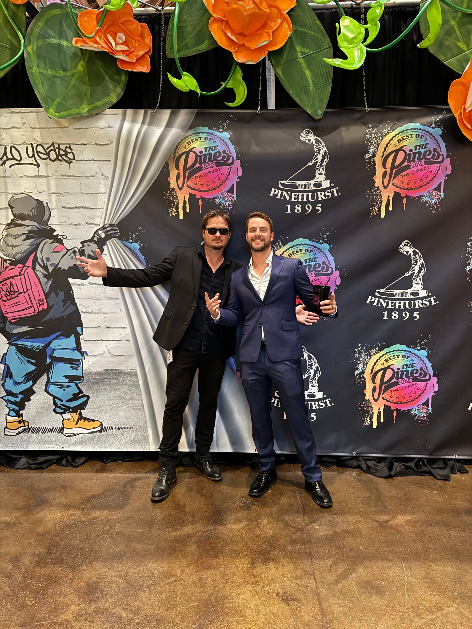 Two men are standing in front of a wall with graffiti on it.