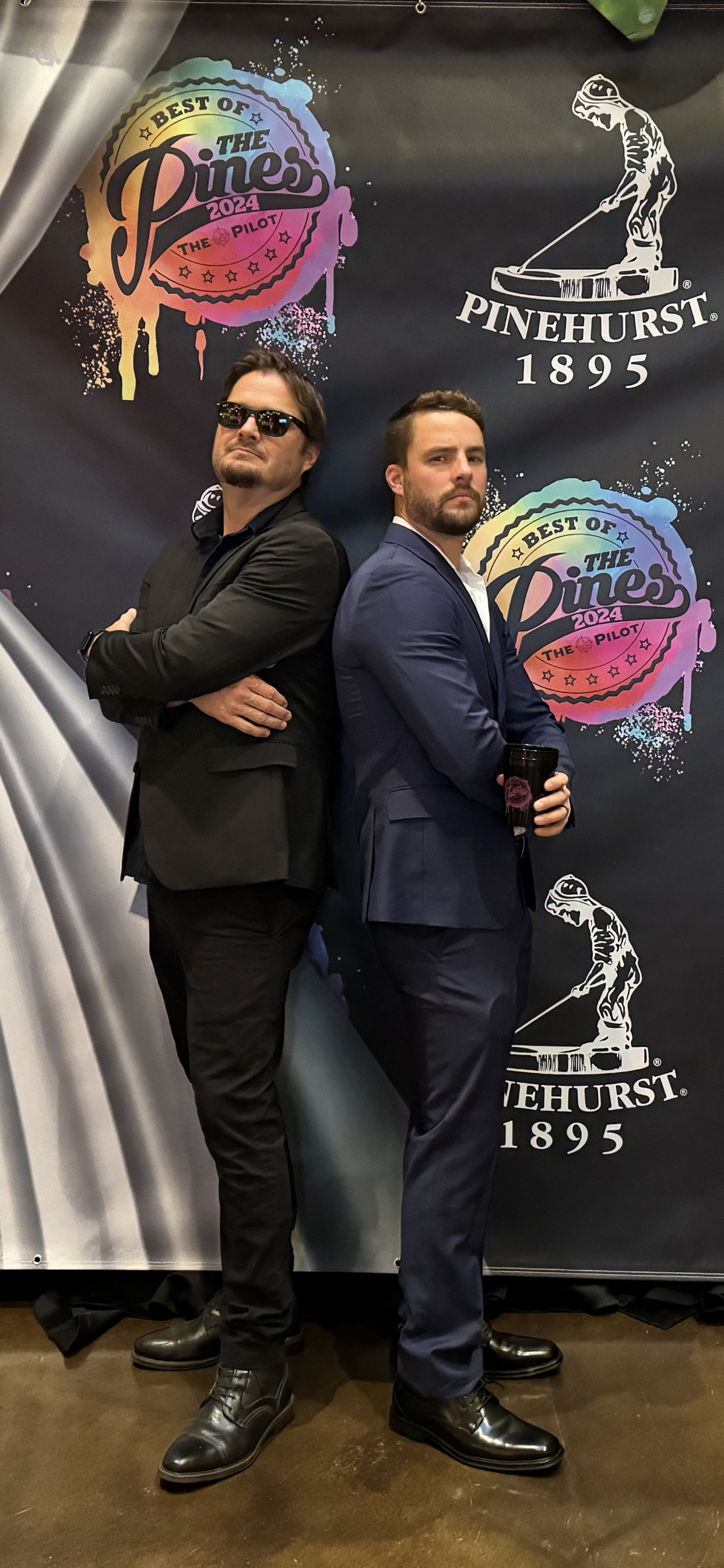 Two men in suits are standing back to back in front of a banner.