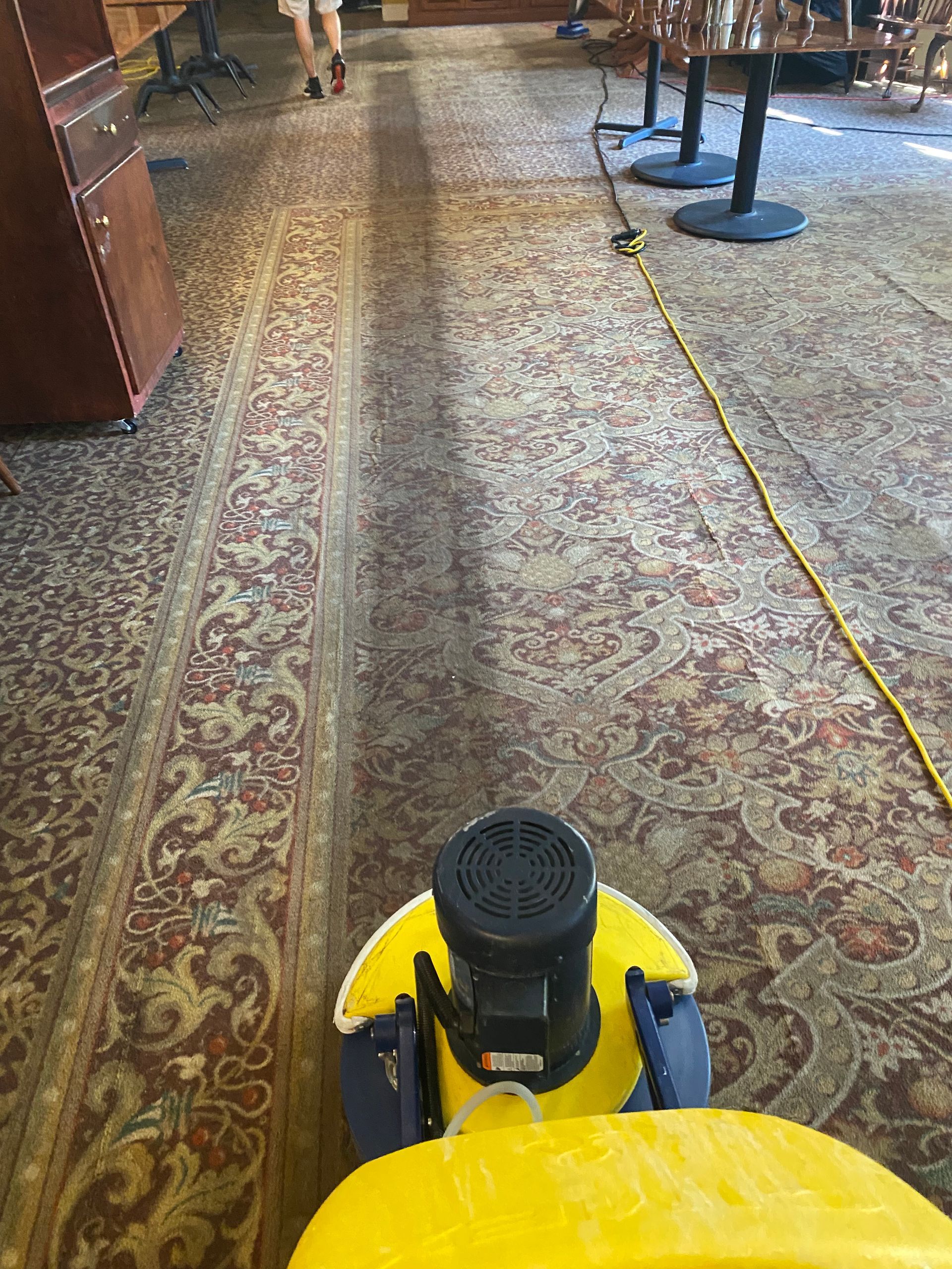 A yellow vacuum cleaner is cleaning a carpet in a room.