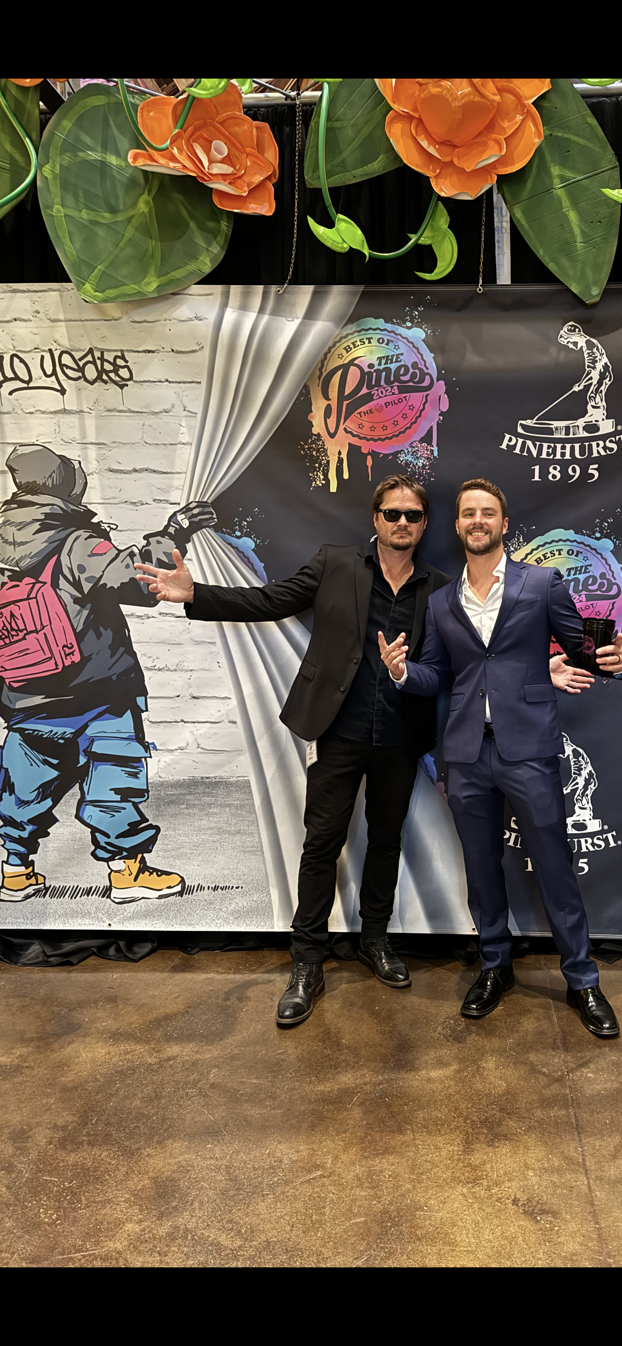 Two men are posing for a picture in front of a painting.