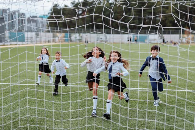 Children running toward a soccer goal on a grassy field, with the net in the foreground.