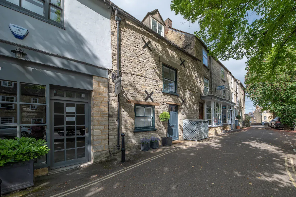 Row of stone buildings on a narrow street. The building on the left has large glass windows and doors.