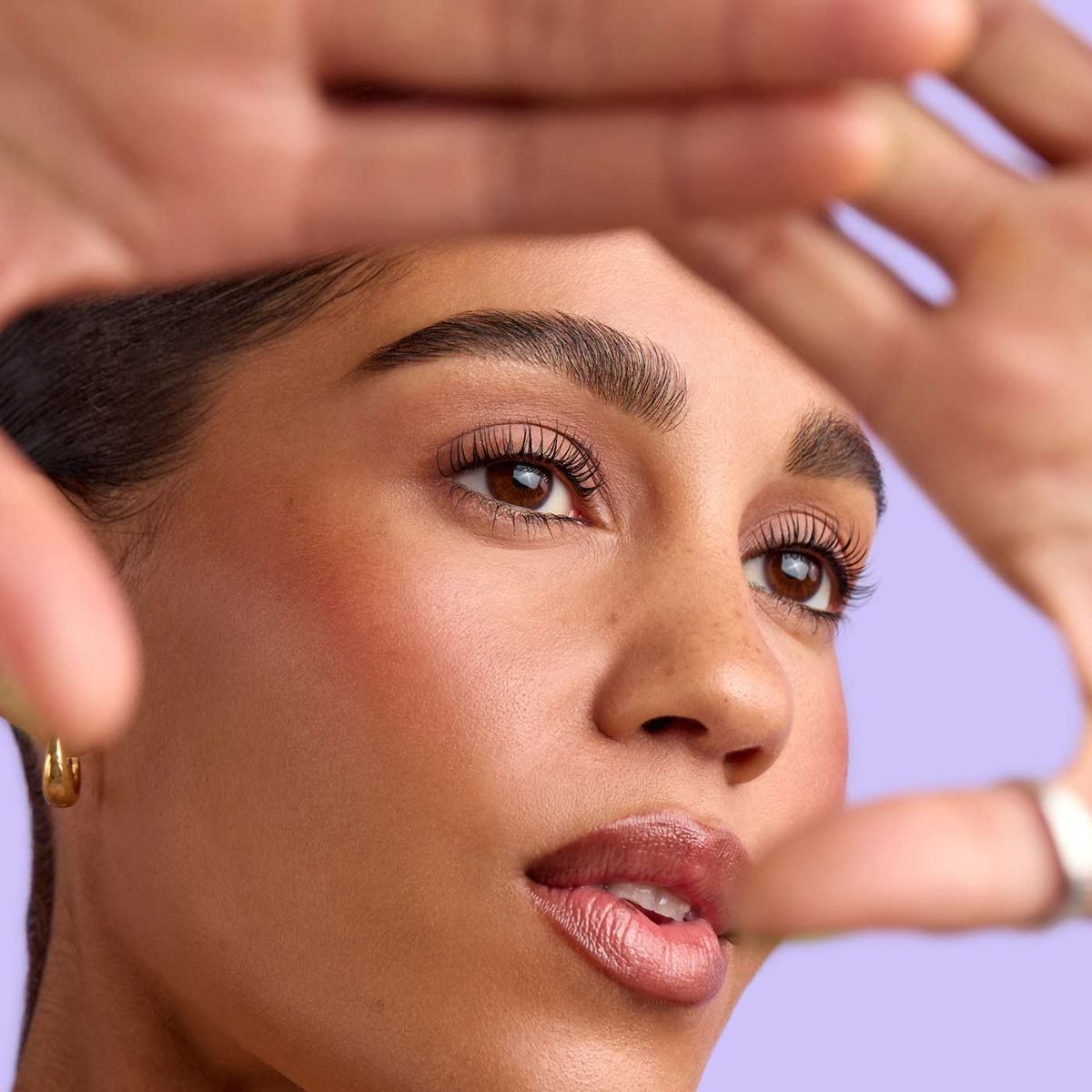 Woman framed by hands, looking up. She has a natural makeup look with full eyebrows, and light pink lips.