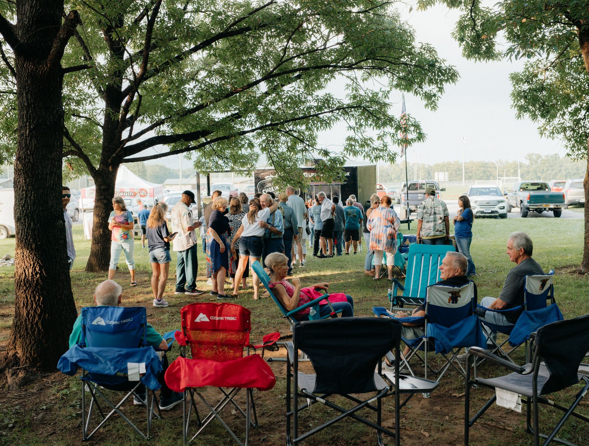 People gathered at an outdoor event, sitting in chairs and standing near a stage.