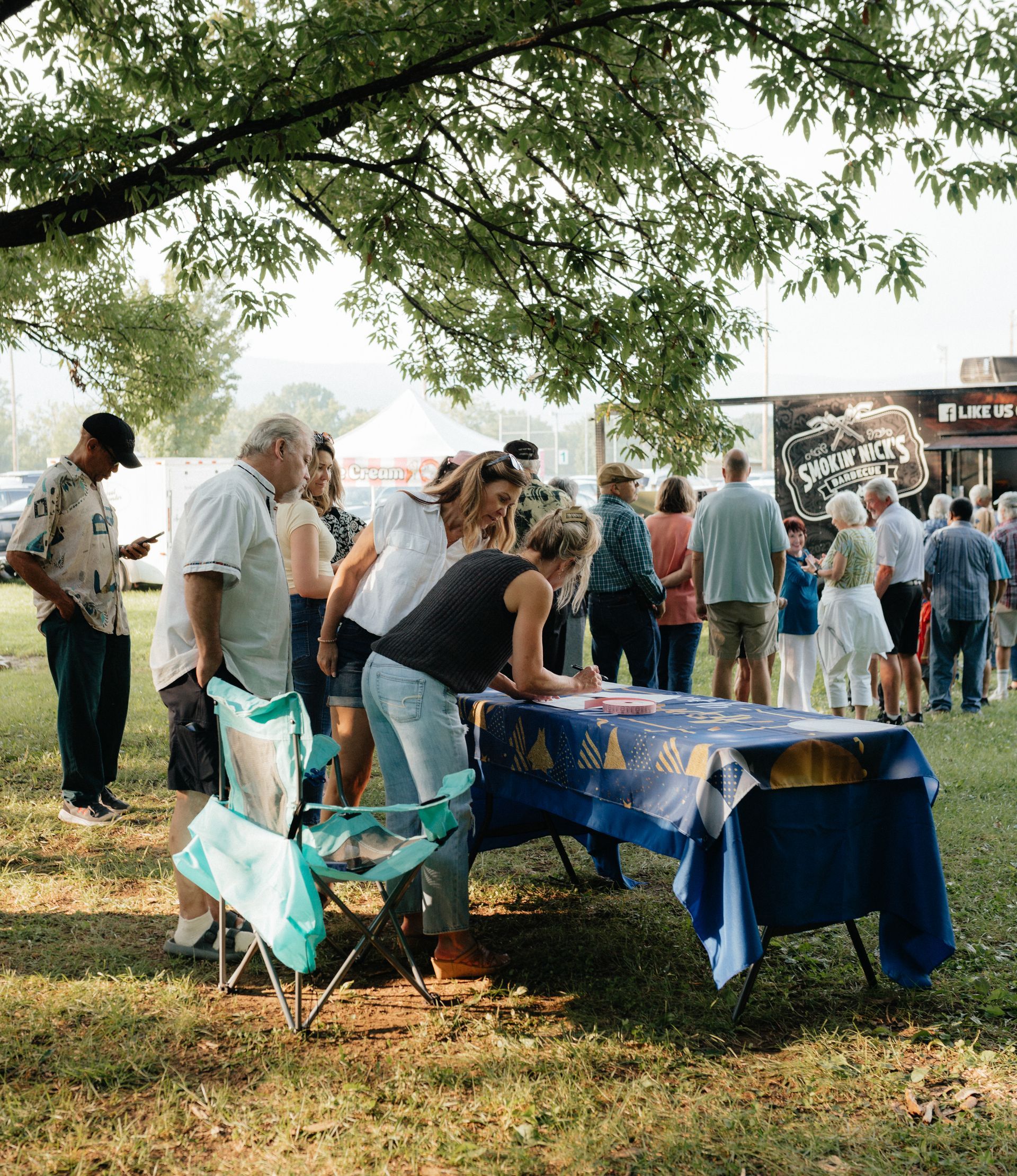 People signing up at an outdoor event. A line of people waits nearby. Blue table with a gold tablecloth.