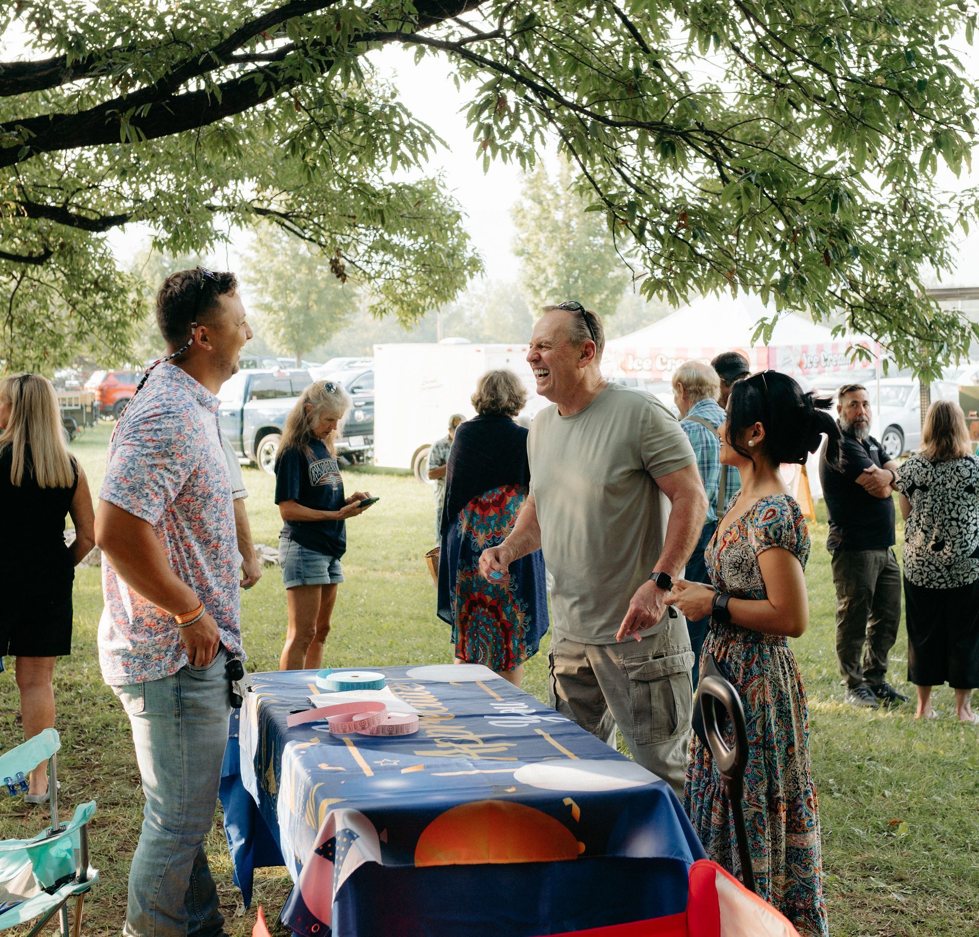 People conversing at an outdoor event; two men and woman are at a decorated table.