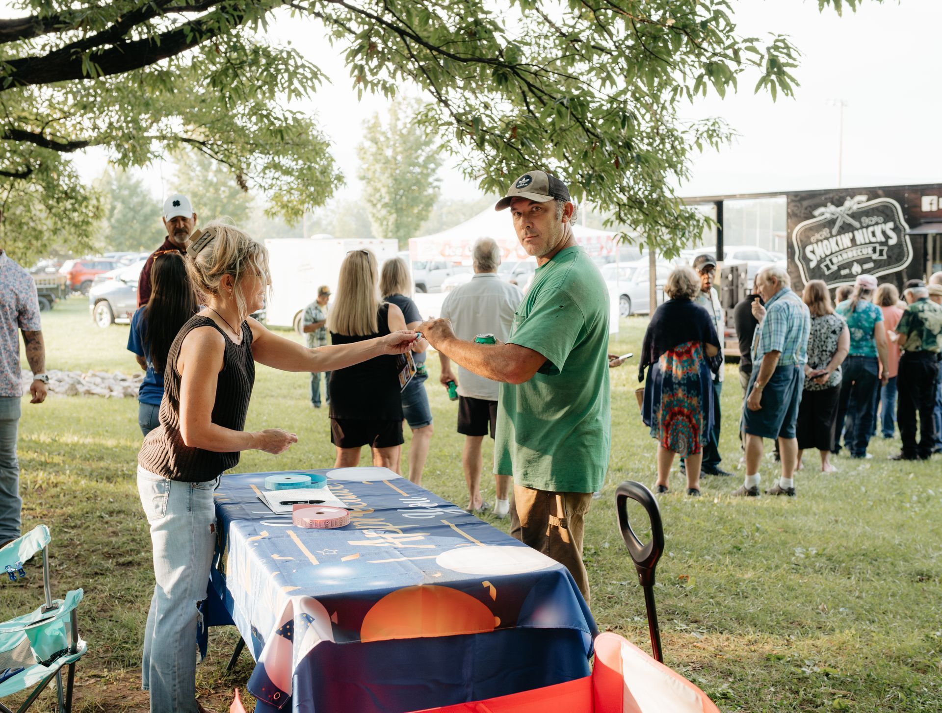 Woman handing a ticket to a man at an outdoor event. Other people queue in the background.