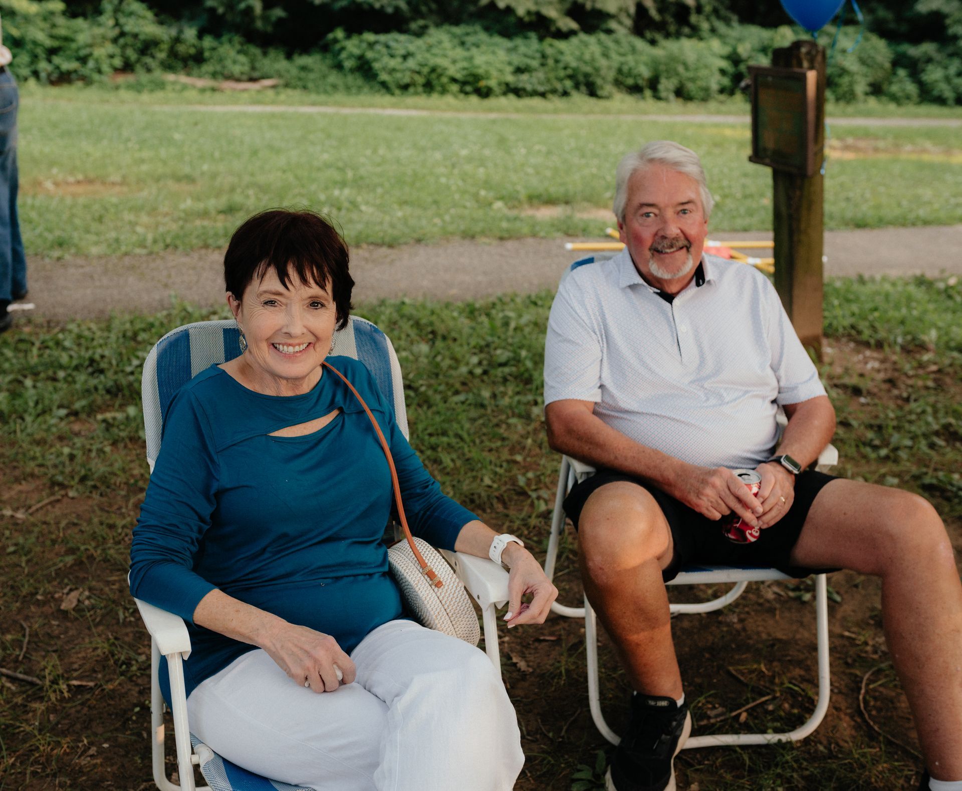 Woman and man in chairs outdoors; woman smiles, blue shirt; man smiles, white shirt, black shorts.