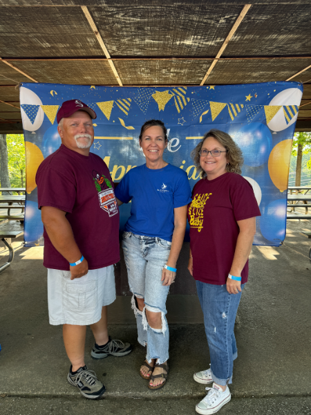 A man and two women are posing for a picture in front of a banner that says happy birthday