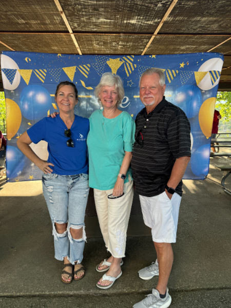 Three people posing for a picture in front of a blue background with balloons