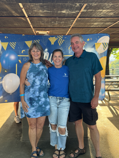 Three people posing for a picture in front of a blue background with balloons