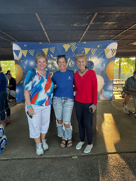 Three women are posing for a picture in front of a blue banner that says 