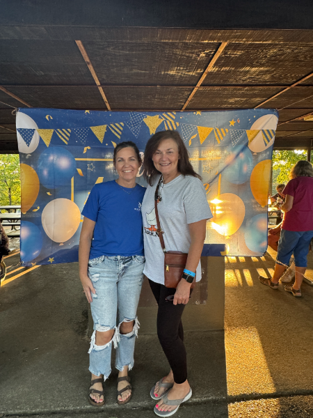 Two women are posing for a picture in front of a banner with balloons on it