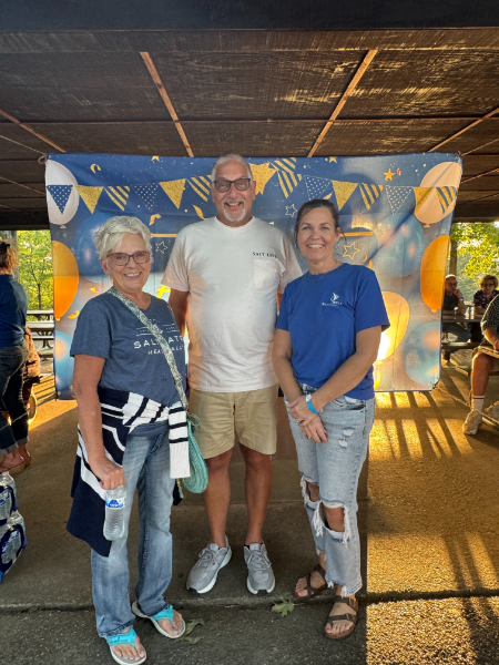 A man and two women are posing for a picture in front of a banner.