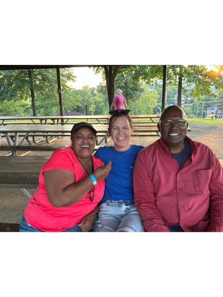 Three people are posing for a picture while sitting at a picnic table.