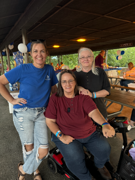 Three women are posing for a picture including one in a wheelchair