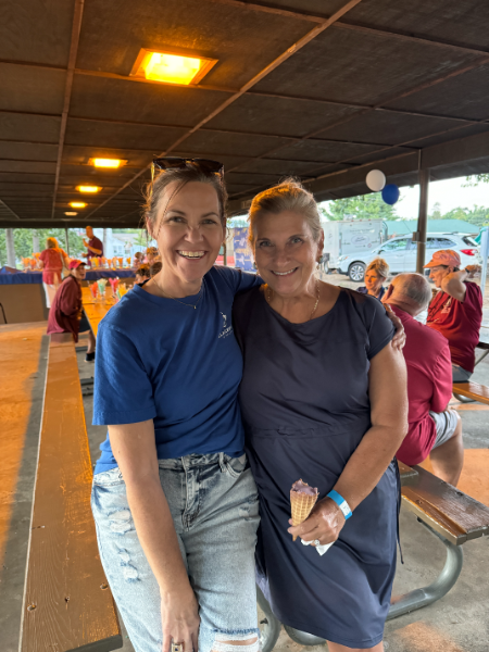 Two women are posing for a picture while sitting at a picnic table.