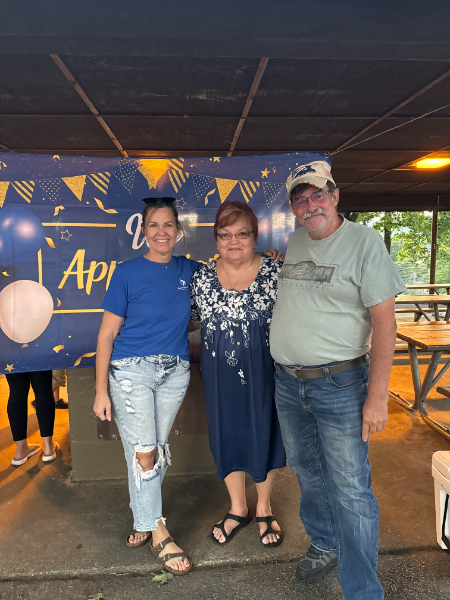 Three people are posing for a picture in front of a sign that says april