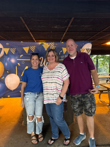 Three people are posing for a picture in front of a wall with balloons.