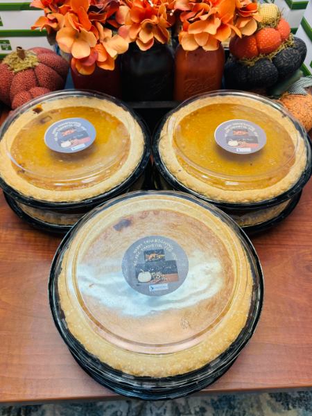 Three pumpkin pies are stacked on top of each other on a wooden table.