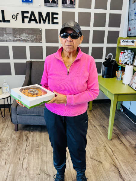 A woman in a pink shirt is holding a box of donuts