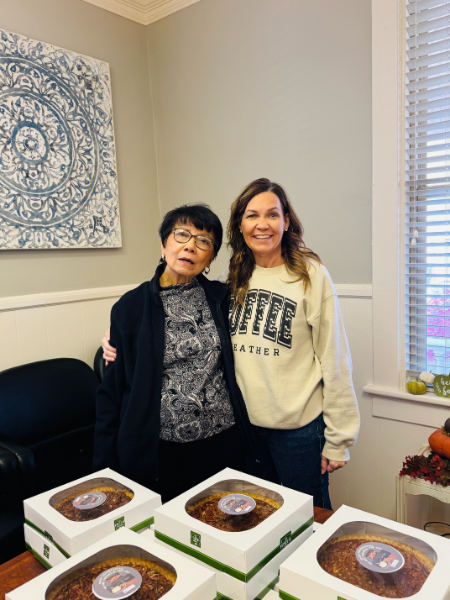 Two women are posing for a picture in front of boxes of cake.