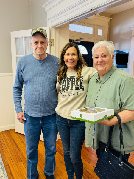 A woman wearing a coffee shirt stands between two men and a woman holding a box