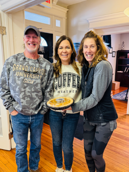 A man and two women are standing next to each other holding a pie.