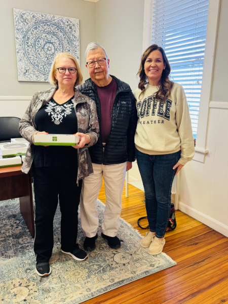 A woman wearing a sweatshirt that says coffee is standing next to two other people