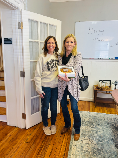 Two women standing next to each other in front of a white board that says happy