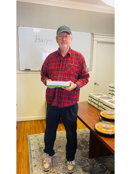 A man in a plaid shirt is holding a box in front of a white board that says happy birthday