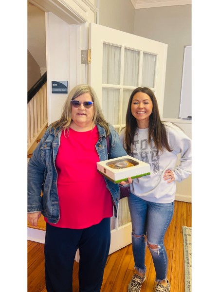 Two women are standing next to each other holding a box of food.