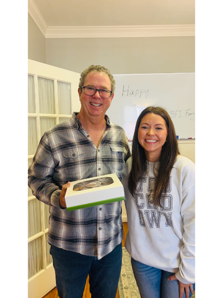 A man and a woman are posing for a picture while the man is holding a cake.