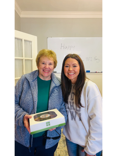 Two women are posing for a picture and one is holding a box.