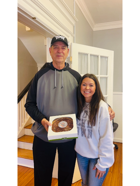 A man and a woman standing next to each other holding a box of donuts