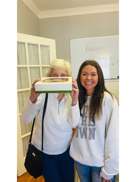Two women standing next to each other holding a cake in front of their faces